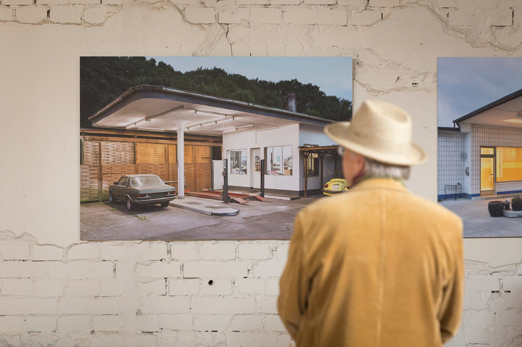 Ein Besucher der ABGETANKT Ausstellung schaut sich auf einem Fine Art Print eine alte Tankstelle an